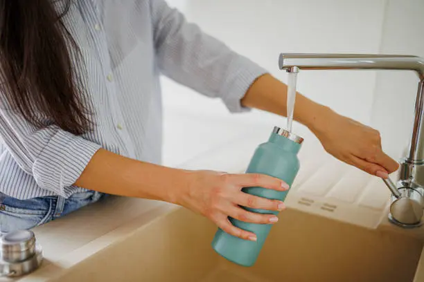 A reusable bottle being refilled at a kitchen tap